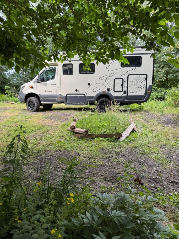 Egal ob voll modern... Ein Wohnmobil steht auf einem Naturgrundstück, umgeben von Bäumen und Pflanzen.